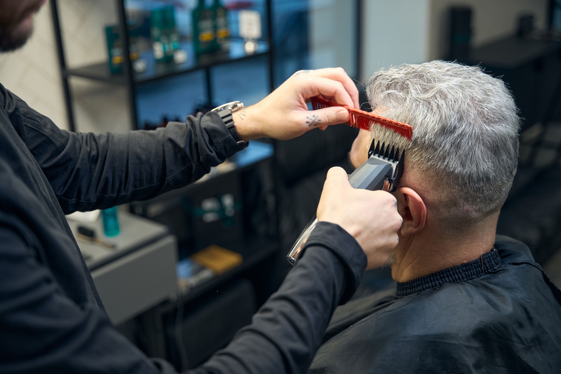 Hairdresser doing a machine haircut to mature client with gray hair